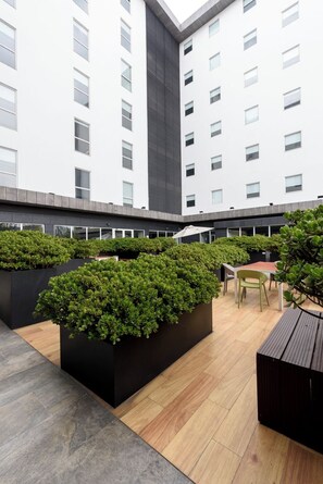 A modern outdoor area with planters, a wooden table, and chairs. - City Express Plus by Marriott Bogota Aeropuerto (Bogotá)