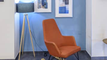 A room with a blue wall, a framed abstract painting, a modern orange chair, and a floor lamp.
