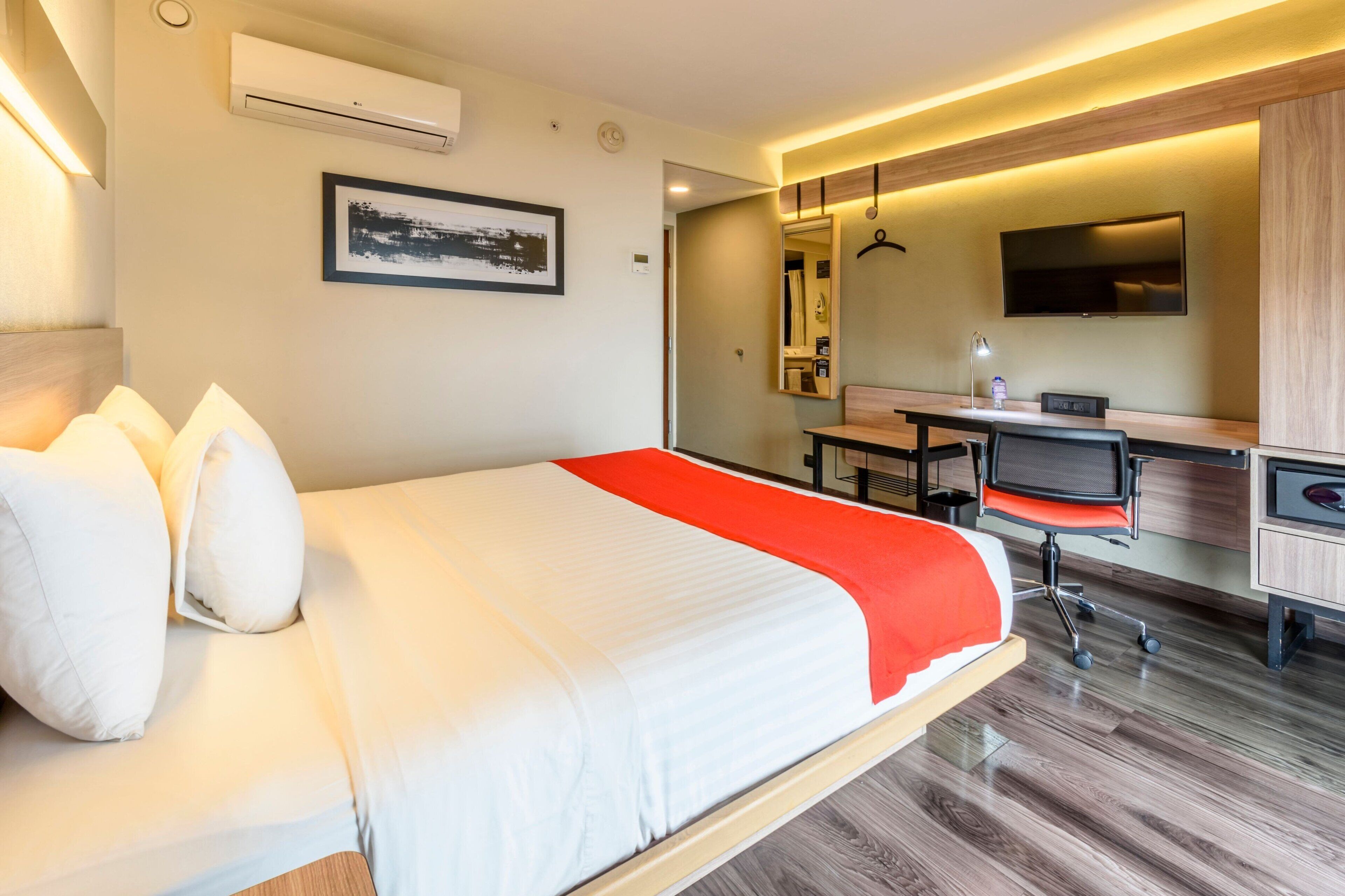 A hotel room with a bed, a desk, a chair, a TV, and a mirror.