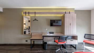 Una habitación de hotel moderna con un escritorio de madera, una silla, un televisor y un armario.