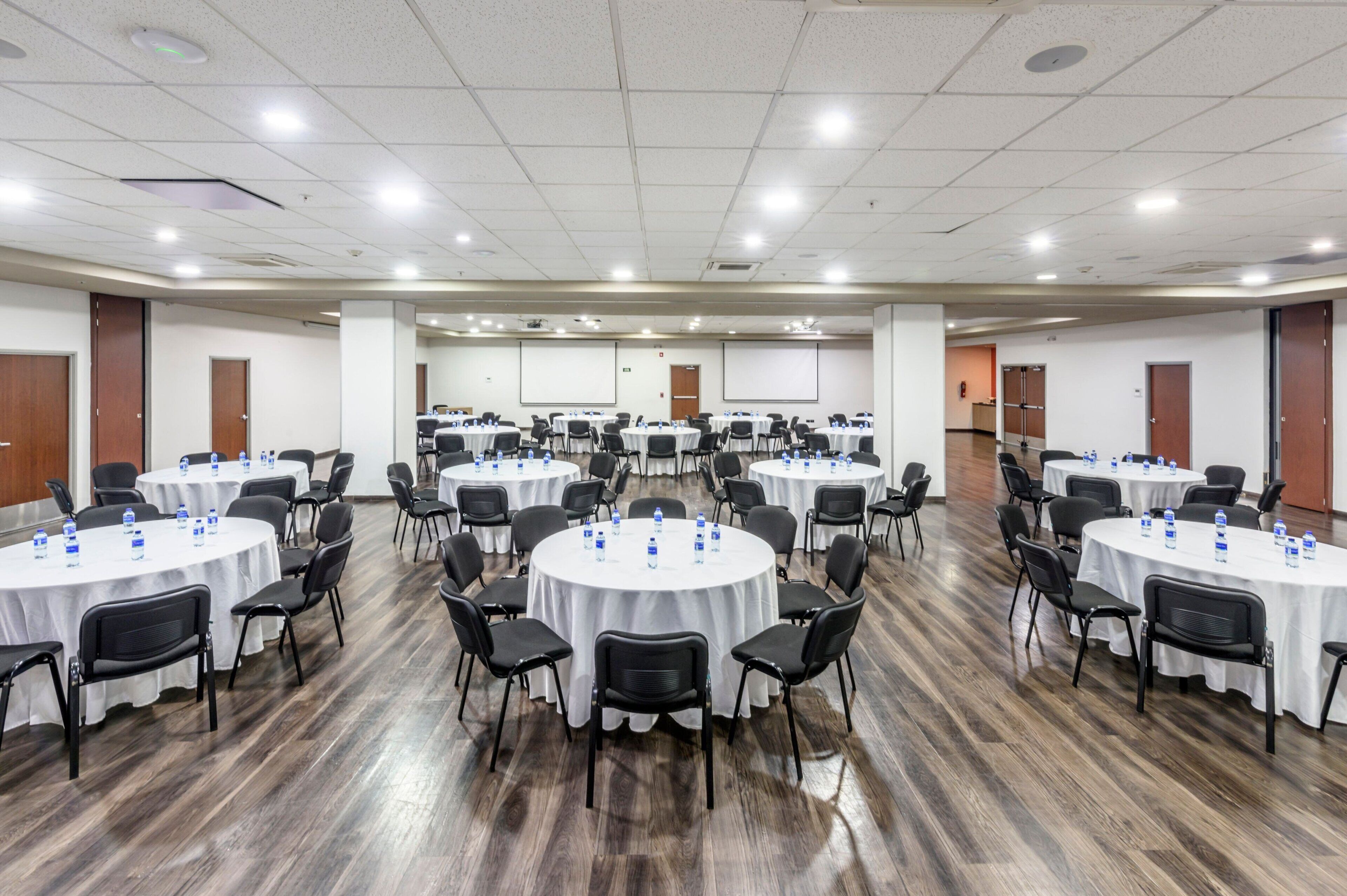 Un salón de conferencias con varias mesas redondas, cada una con sillas y botellas de agua.