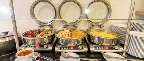 A buffet with three stainless steel chafing dishes containing different foods, a bowl of soup, and a stack of plates.