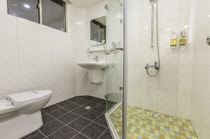 Un baño con inodoro, lavamanos y zona de ducha con mampara de vidrio.