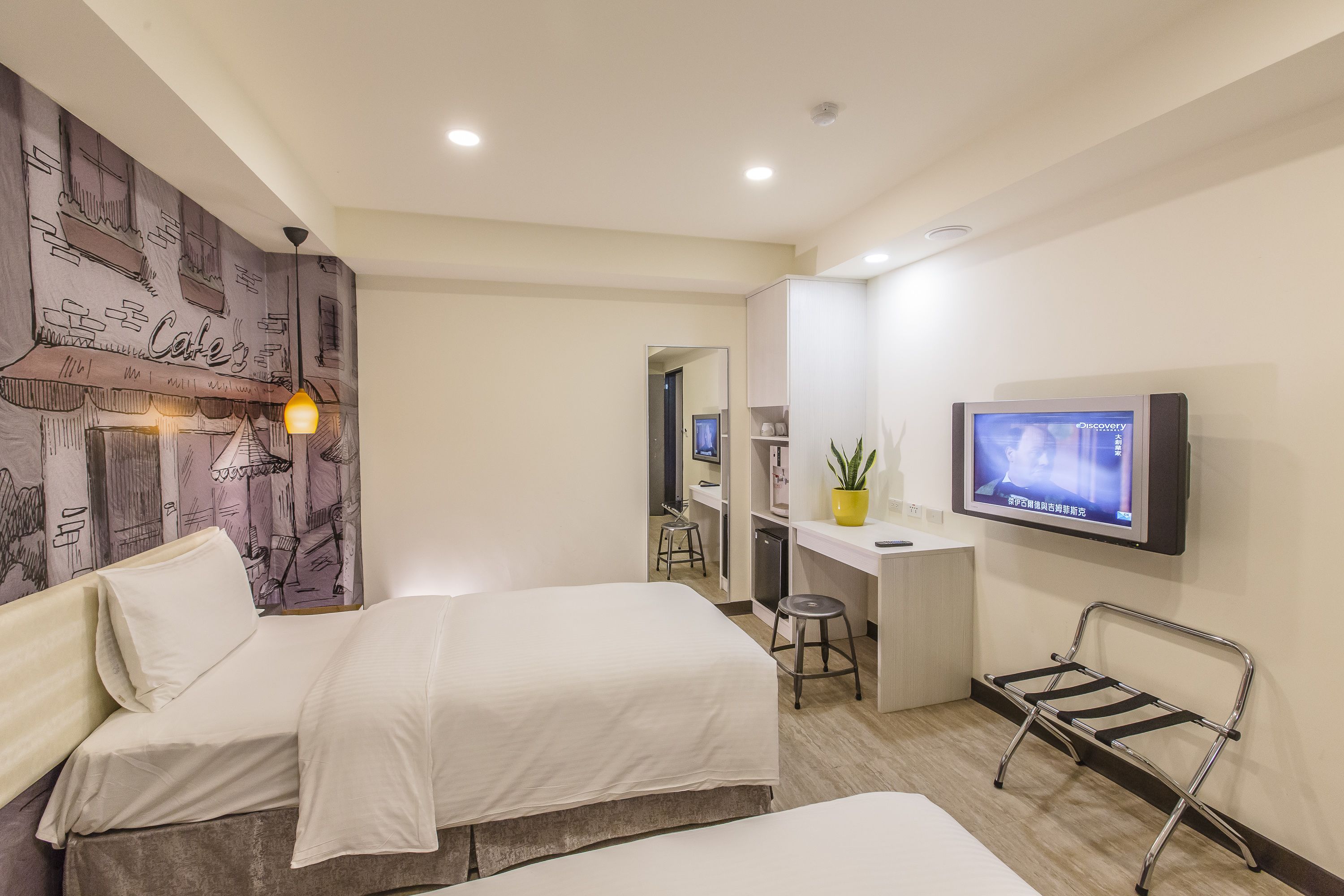 A hotel room with two beds, a desk, a TV, and a bathroom visible through an open door.