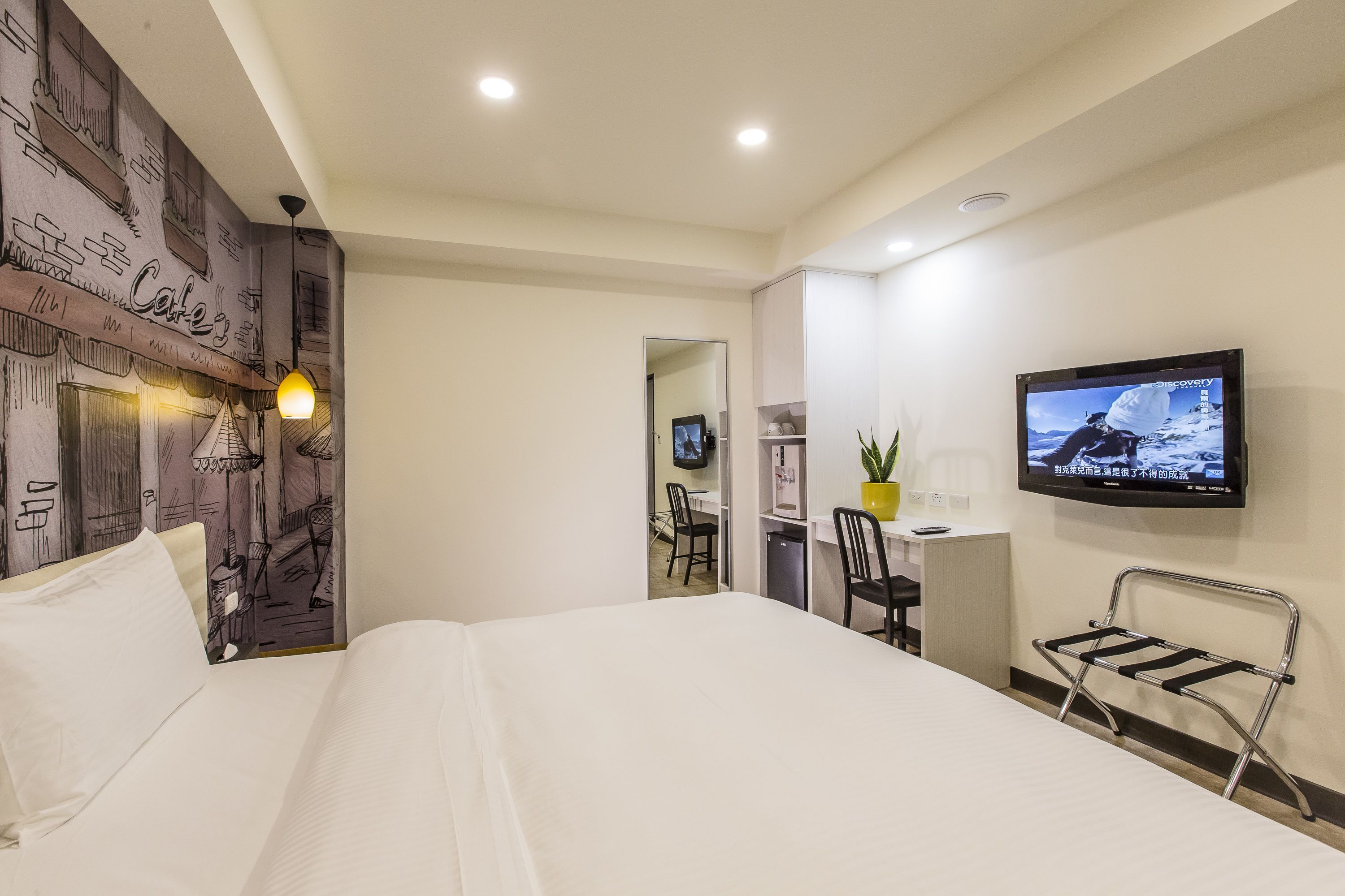Una habitación de hotel con cama, escritorio, silla, televisor y un mural en la pared.