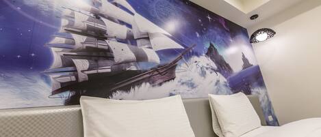 A bedroom with a large wall mural of a ship sailing on water, a bed with white bedding, and a modern ceiling light fixture.