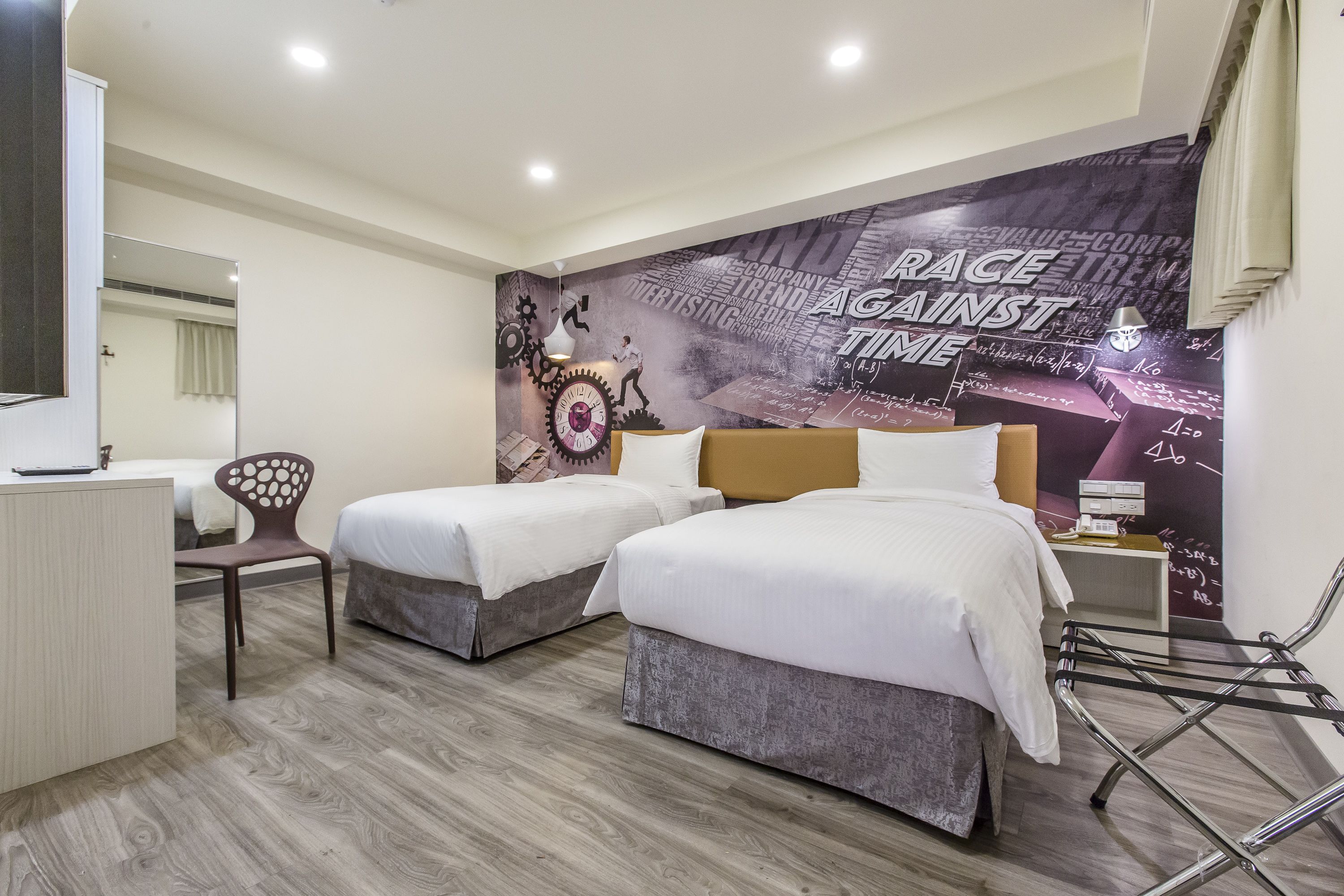 Une chambre d’hôtel avec deux lits, un bureau et un miroir. La chambre est décorée d’une affiche motivante au mur et possède un plancher en bois.