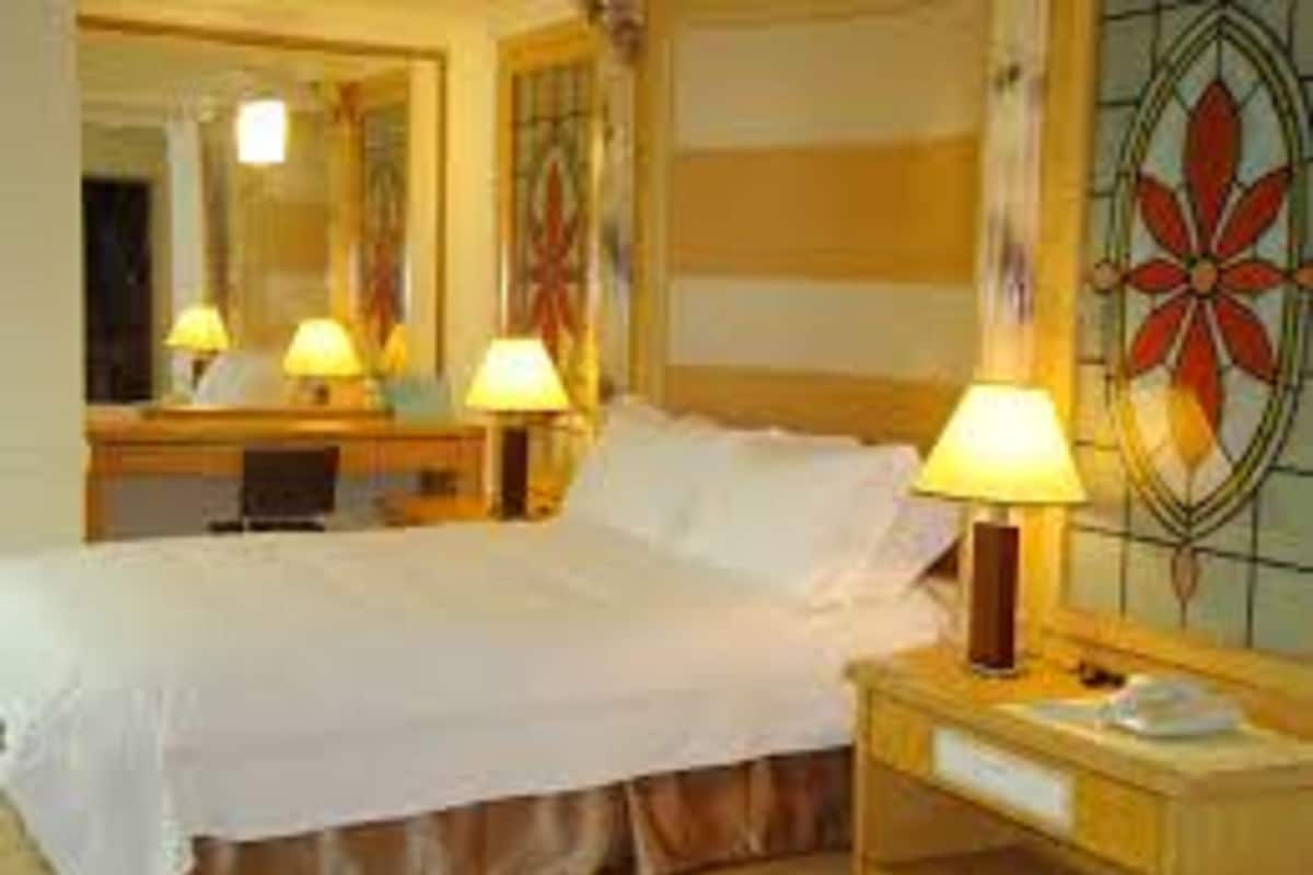 Hotellihuone, jossa on sänky, yöpöytävalaisimet, peili ja koristeellinen seinäpaneeli.