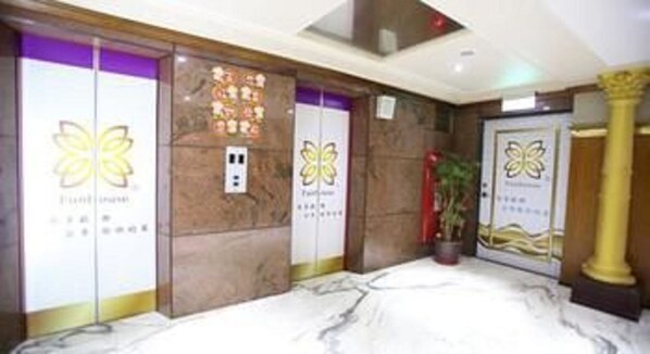 A hotel lobby with marble flooring, a reception desk, and a wall with a floral logo.
