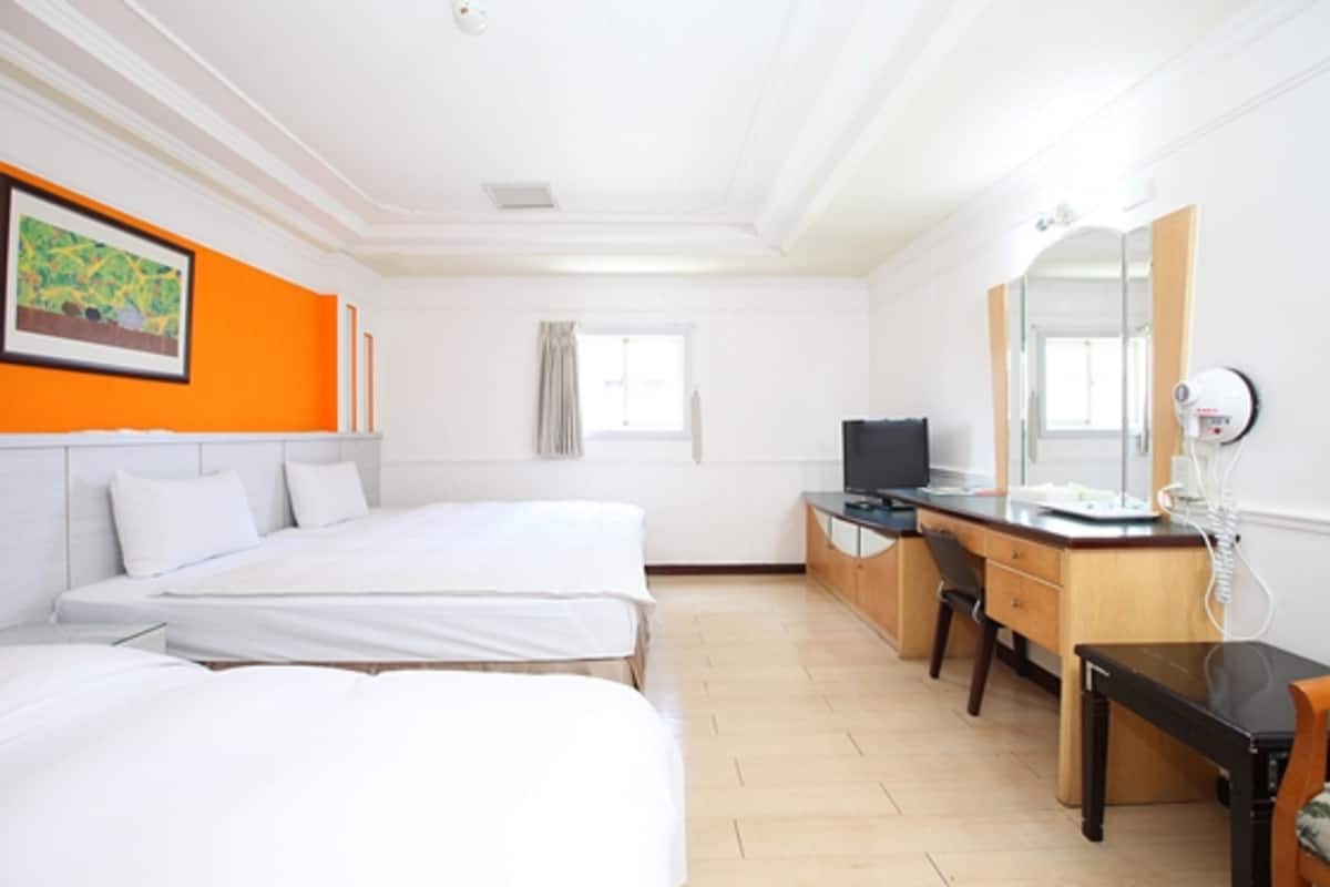 Hotellihuone, jossa on kaksi sänkyä, työpöytä, tuoli, televisio ja peili.