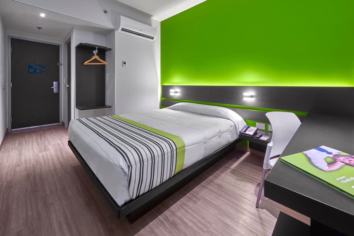 A modern hotel room with a bed, a desk, and a green accent wall.