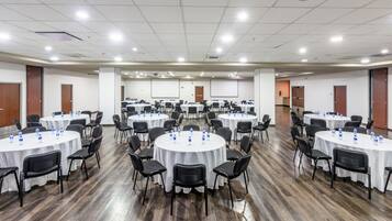 Un salón de conferencias con varias mesas redondas, cada una rodeada de sillas y equipada con botellas de agua.