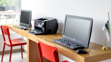 Un espacio de trabajo con una computadora portátil, un ordenador de escritorio, una impresora y dos sillas rojas.