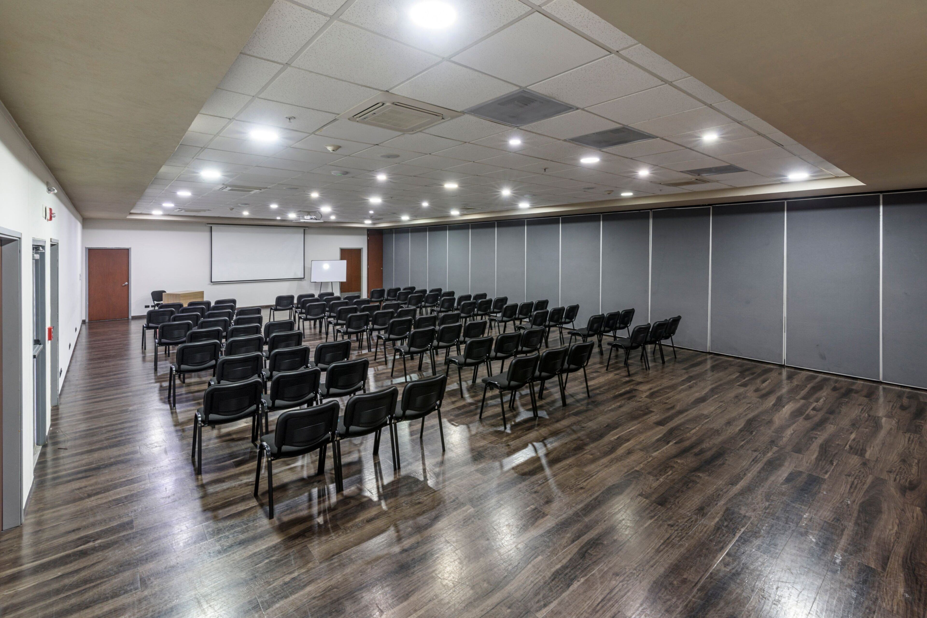 Una sala de conferències amb files de cadires, una pissarra i una pantalla de projector.
