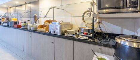 Disposición de bufé con microondas, varios recipientes de comida y máquina de café.