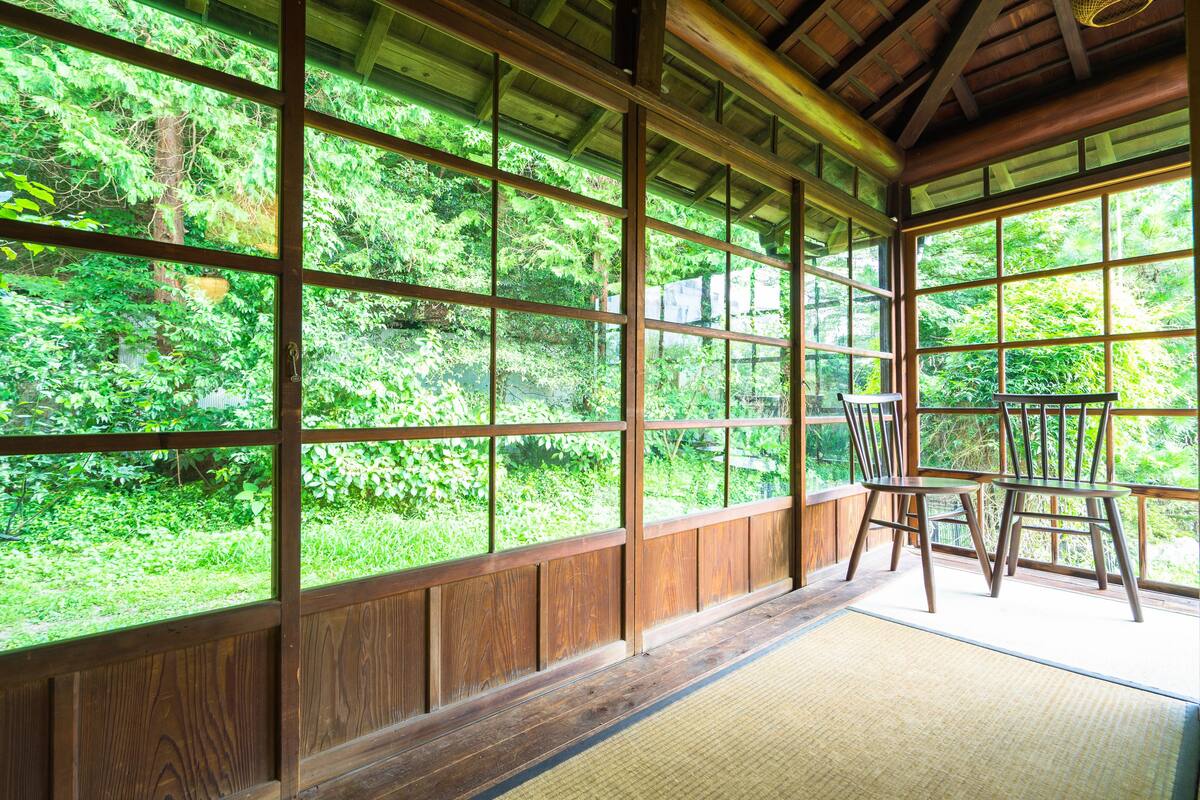 A traditional Japanese room with tatami flooring, wooden sliding doors, and a view of lush greenery outside.