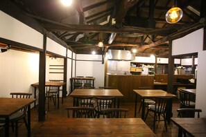 A restaurant with wooden tables and chairs, a kitchen in the background, and hanging light fixtures. - KITAYA Ryokan －Cultural Heritage Inn (Yokohama)