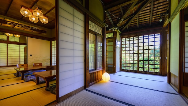 Una habitación japonesa tradicional con suelo de tatami, una mesa baja con cojines y puertas correderas.