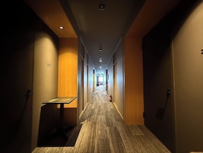 Een hotelgangen met een tapijtvloer, houten wanden en een tafel aan de linkerkant.