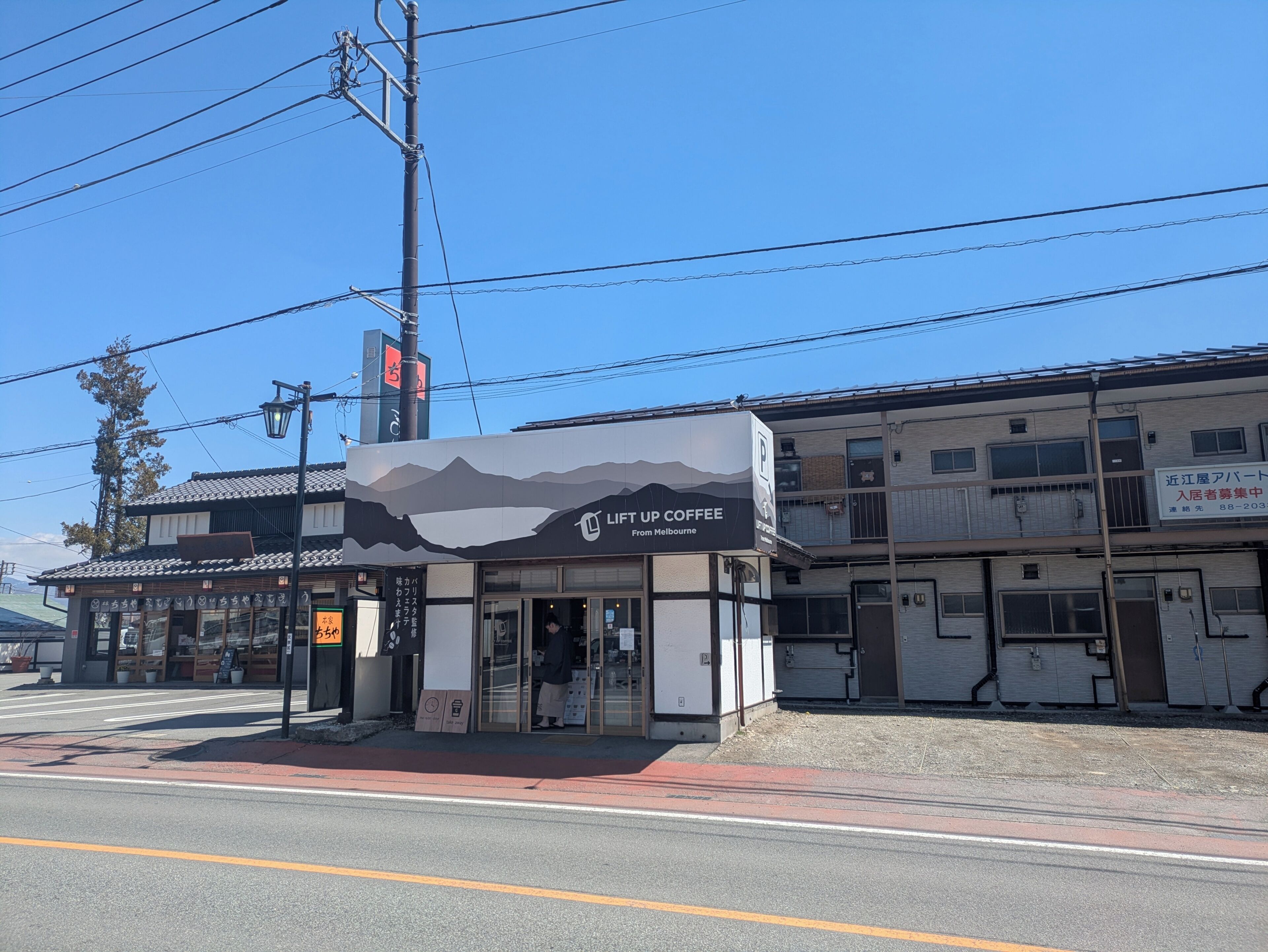 A coffee shop with a mountain graphic on the facade, located at a street corner with a clear sky.
