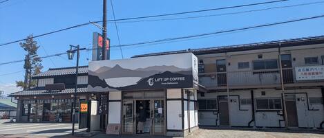 Un café dont la façade est ornée d’un motif représentant une montagne, situé à l’angle d’une rue, avec un ciel dégagé au-dessus.