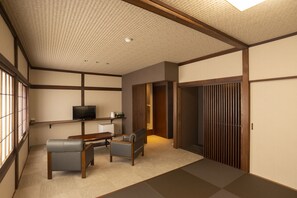 Een traditionele Japanse kamer met tatami vloerbedekking, een lage tafel, twee stoelen, een televisietoestel en schuifdeuren.