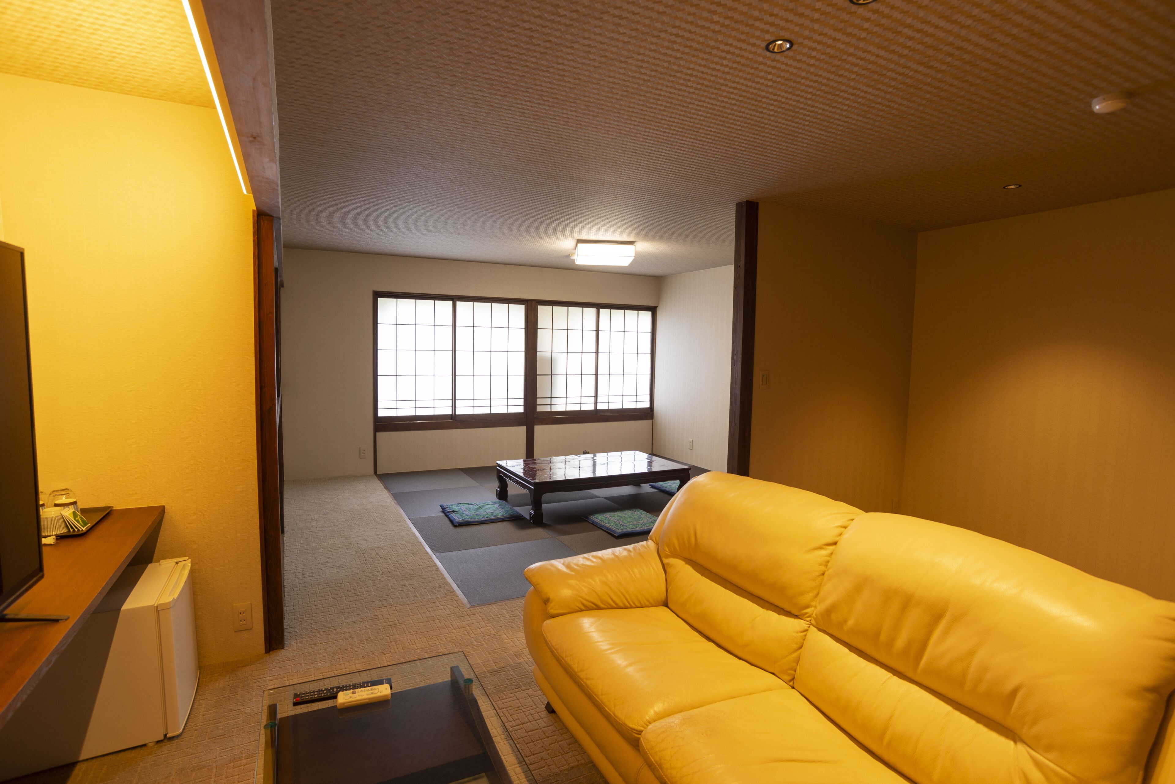 A room with a yellow sofa, a small table, and a television.