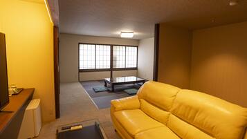 A room with a yellow sofa, a small table, and a television.