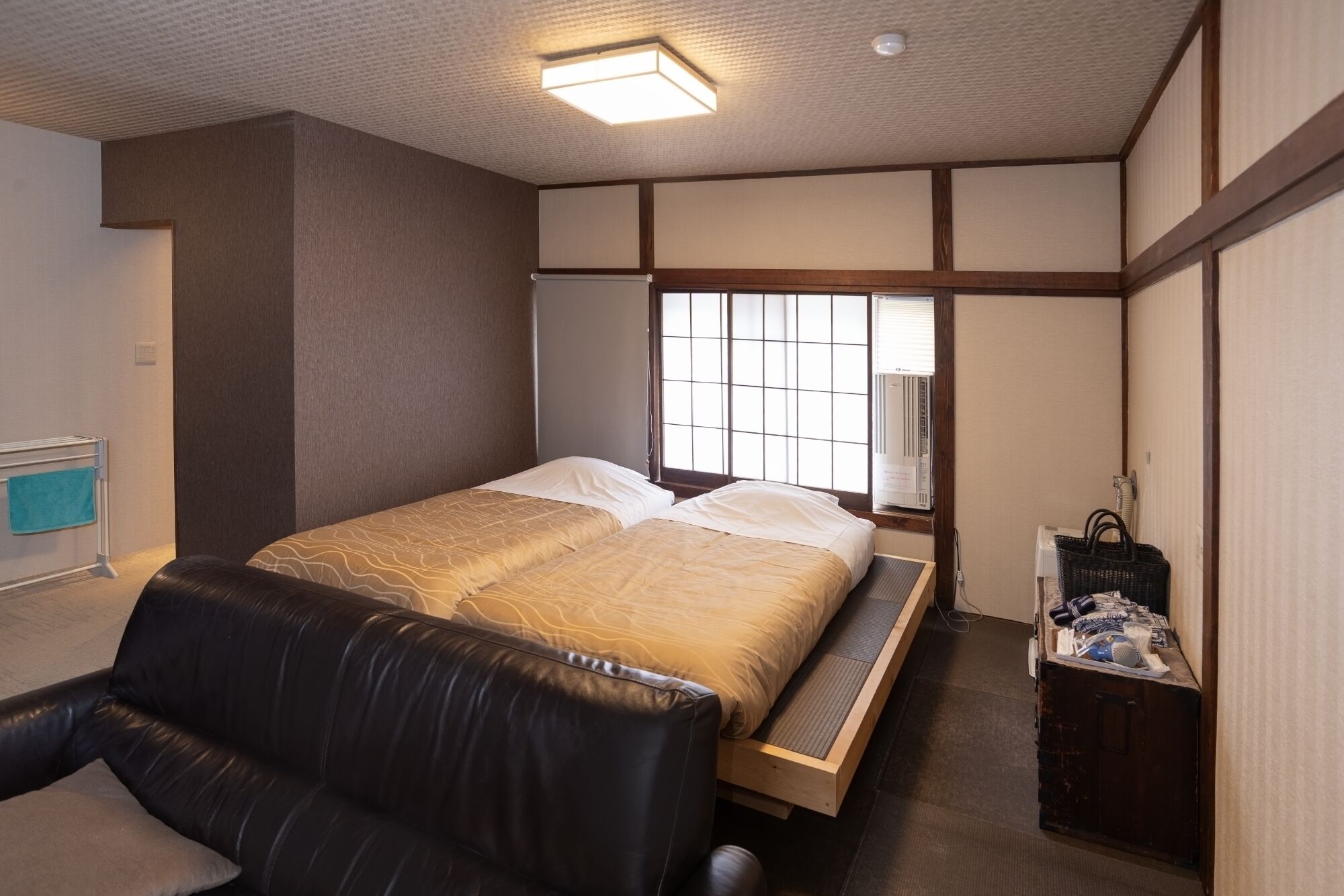 A hotel room with a bed, a seating area, a window, and a small wooden cabinet.