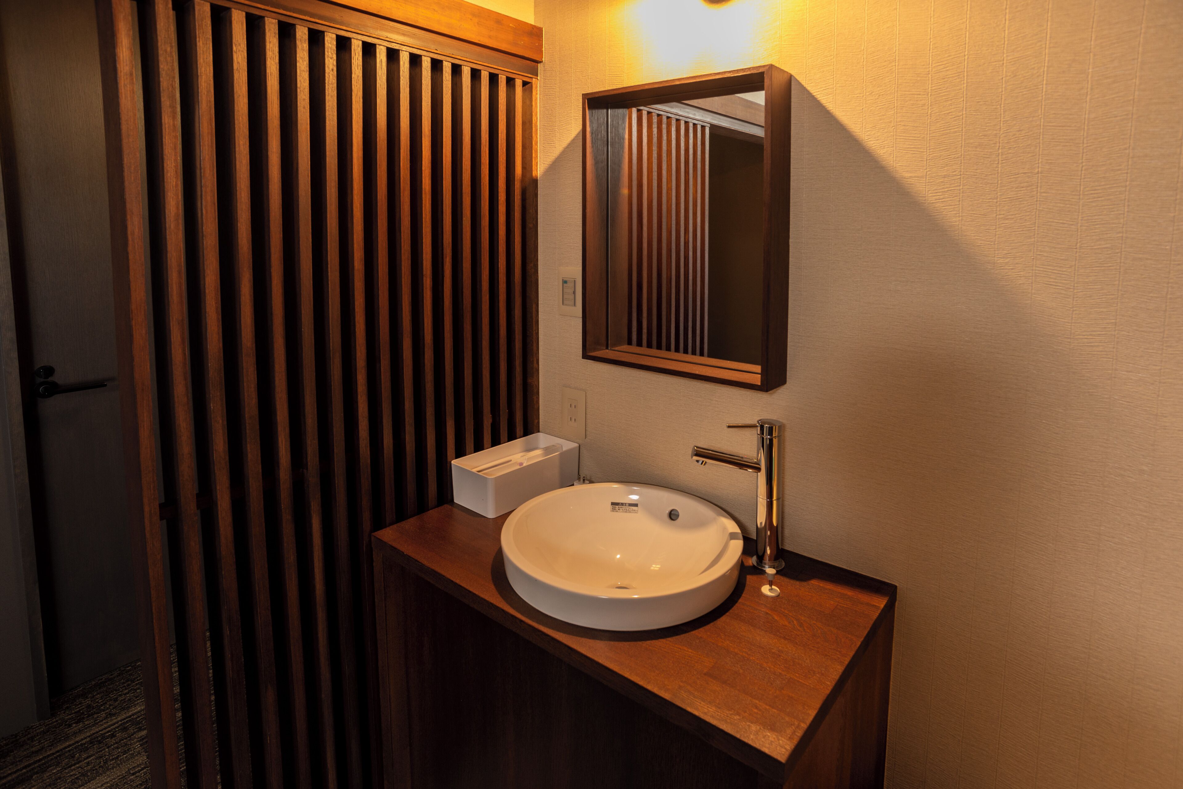 A bathroom with a wooden vanity, a white sink, and a mirror.