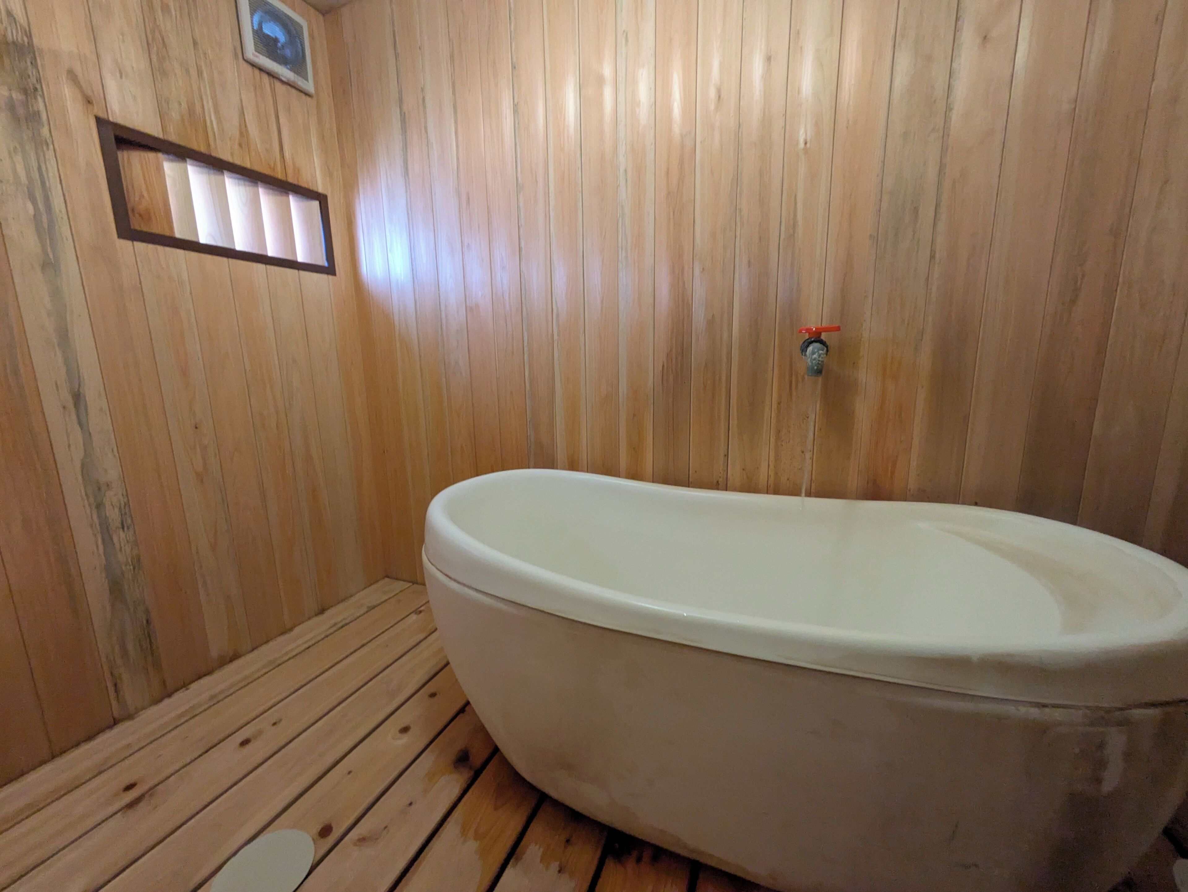 Une pièce aux murs lambrissés, avec une baignoire blanche et une petite fenêtre.