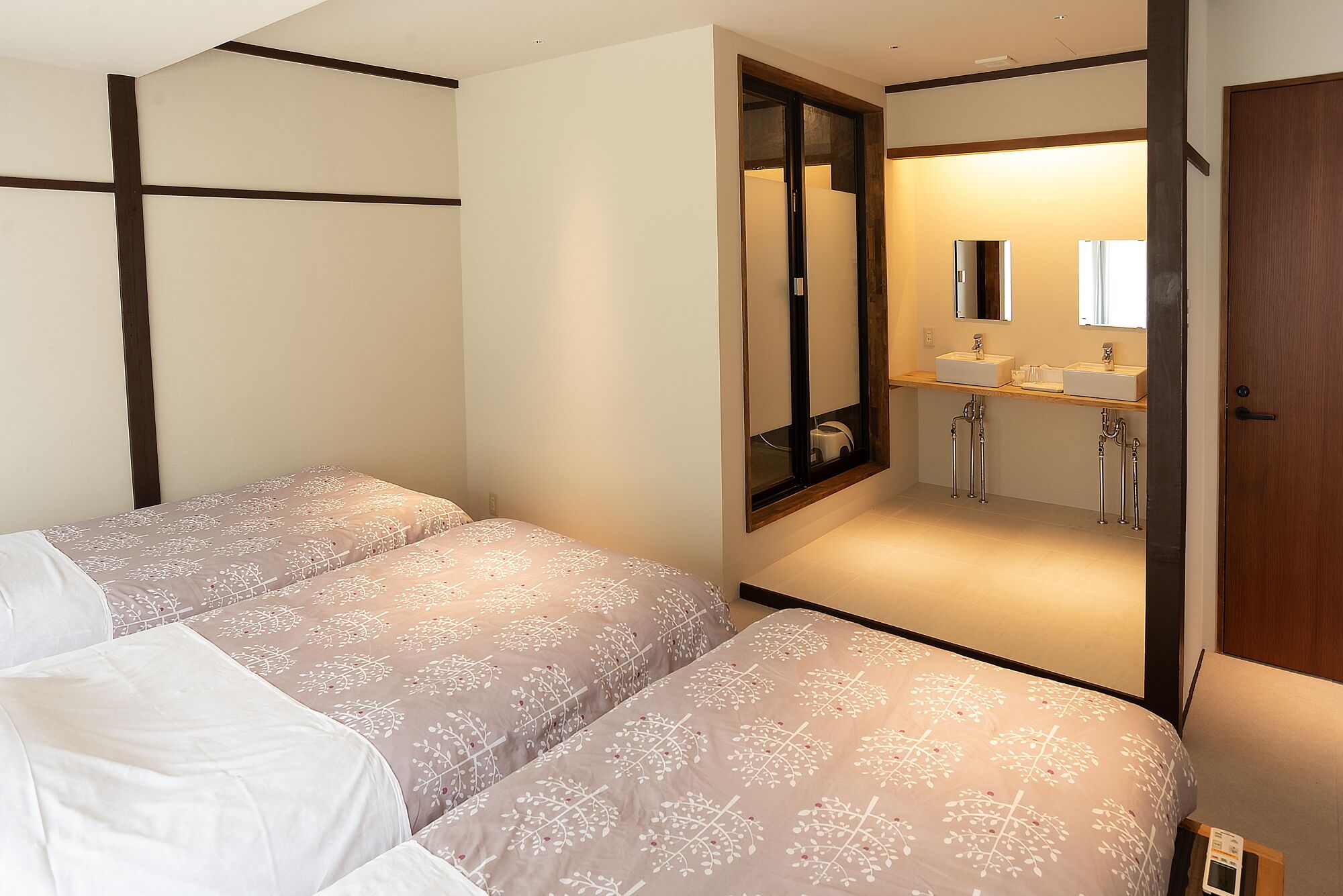 A bedroom with two beds, a bathroom with a mirror, and a wooden door.