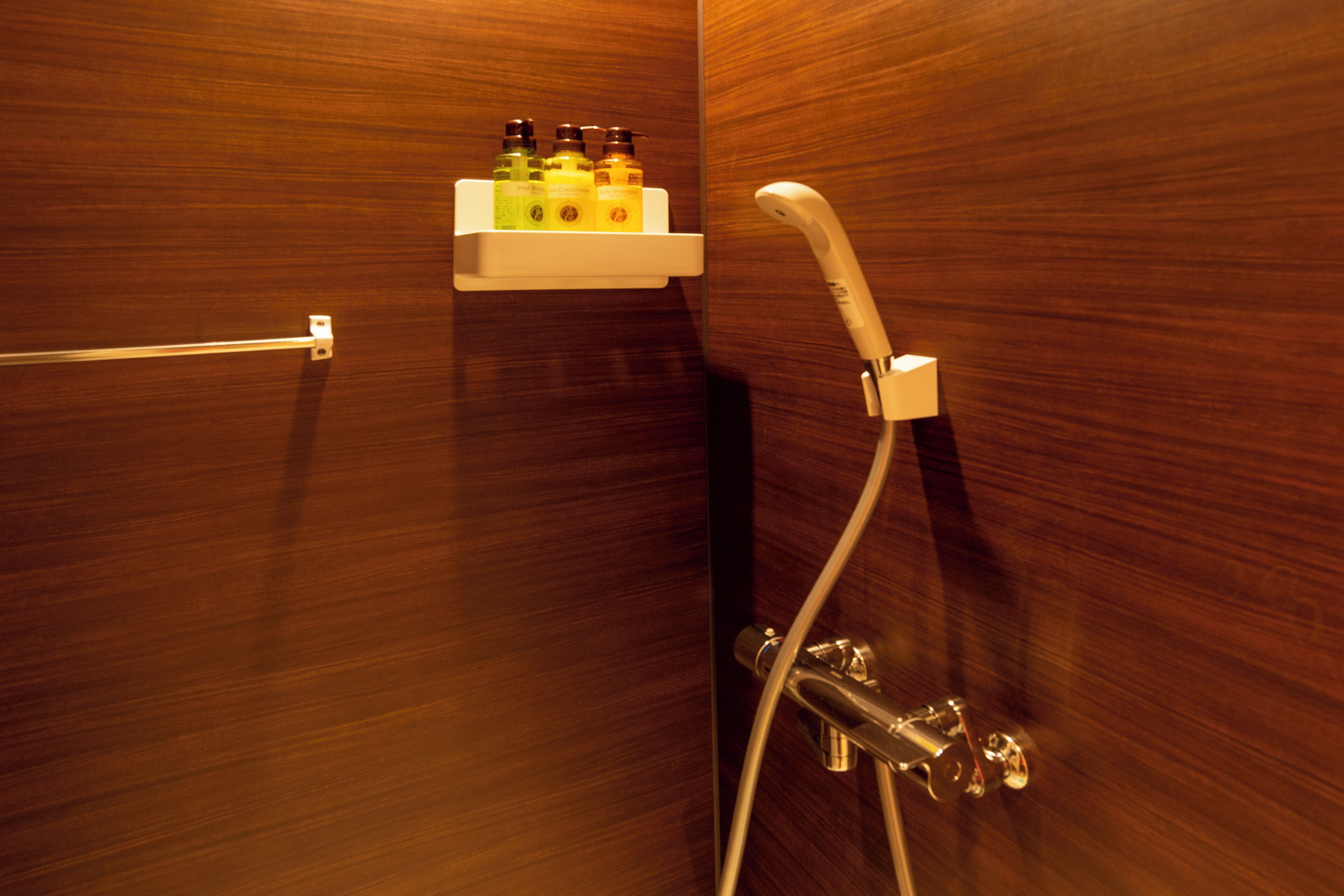 A wooden bathroom with a shower, a white shelf with toiletries, and a towel rack.