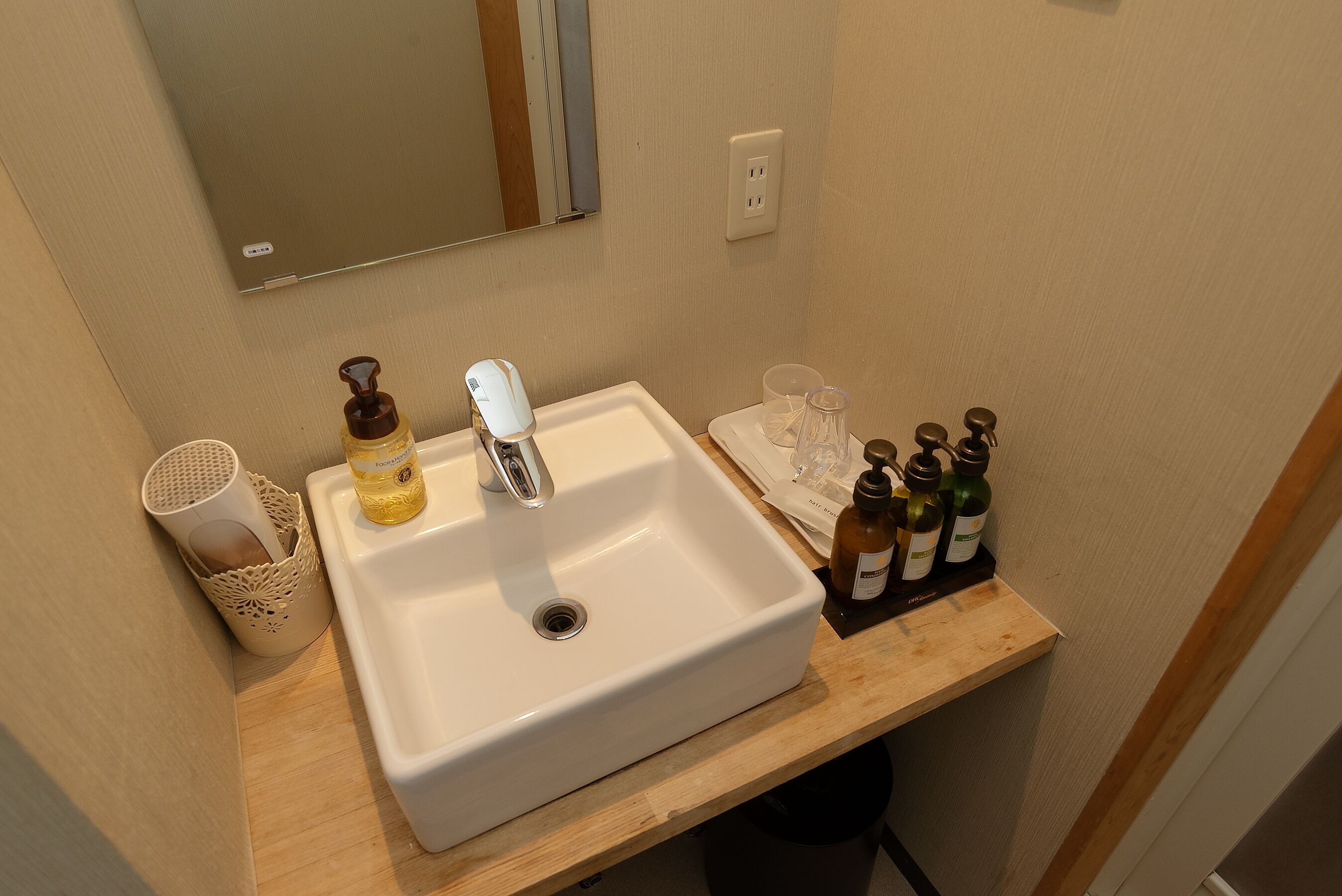 Un lavamanos de baño con un espejo encima, un dispensador de jabón y una botella de jabón líquido en la encimera.