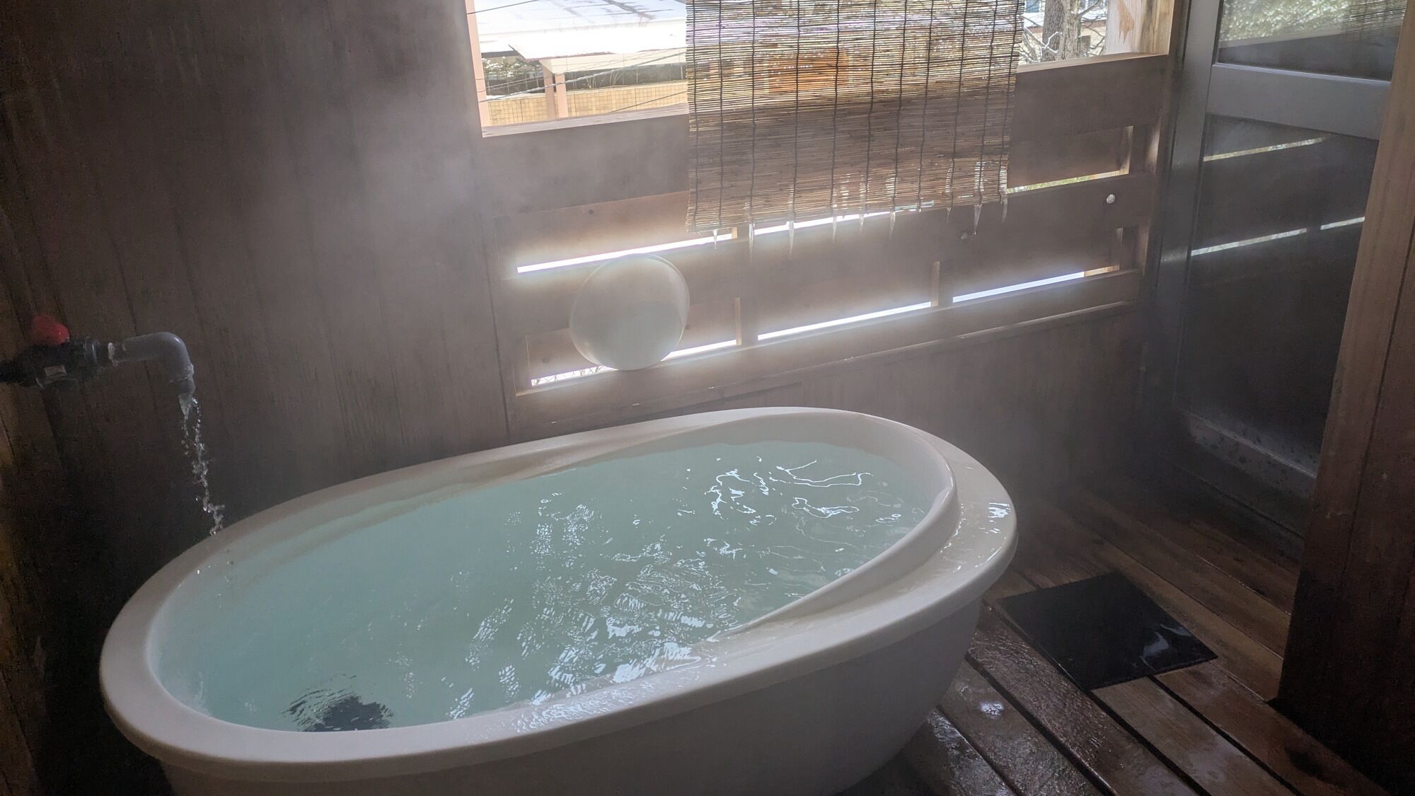 A bathroom with a bathtub, a window with blinds, and a shower area.