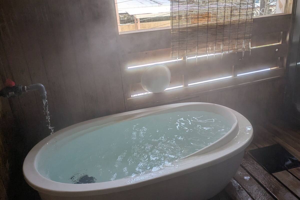 A bathroom with a bathtub, a window with blinds, and a shower area.