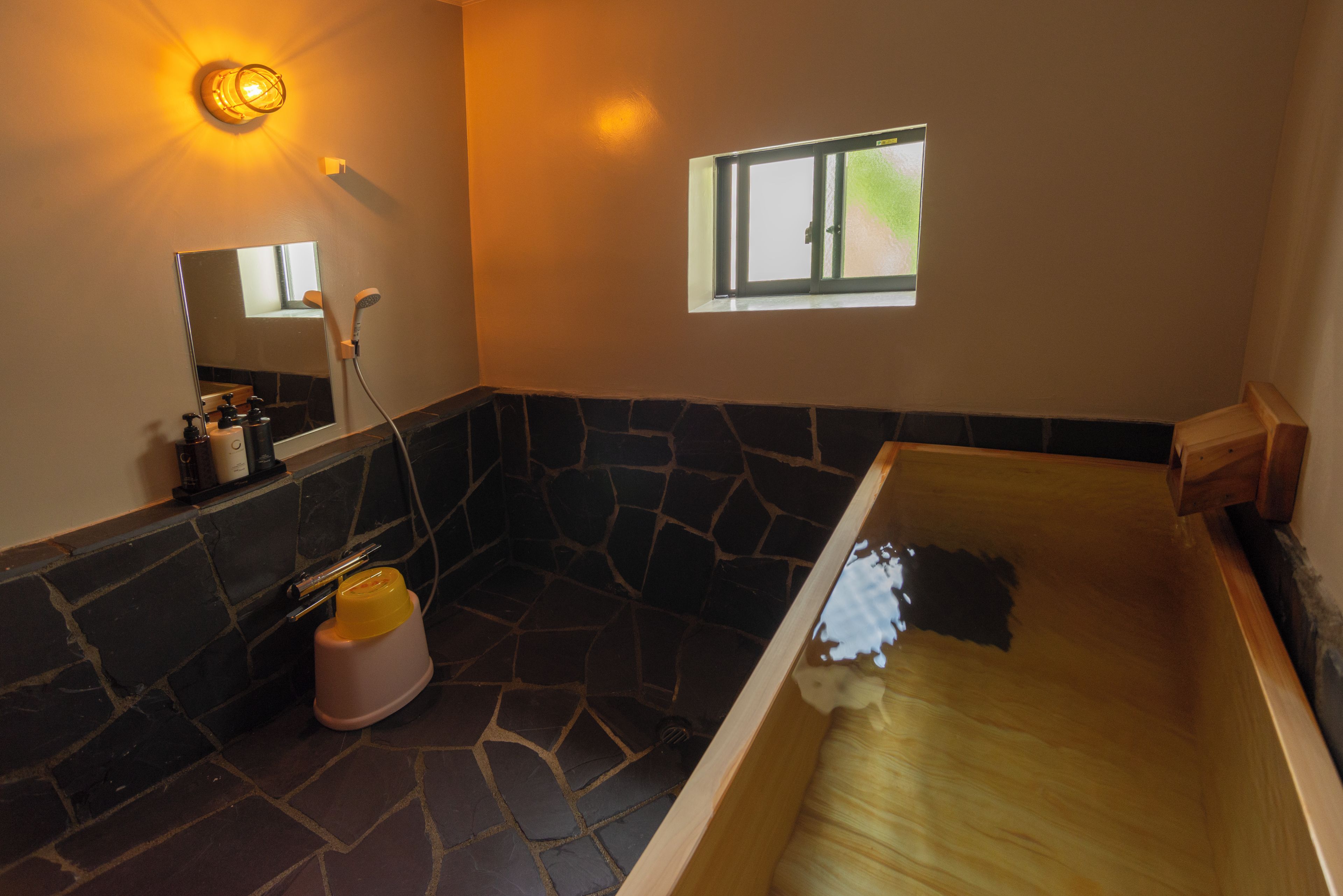 A bathroom with a stone wall, a bathtub, a shower, and a window.