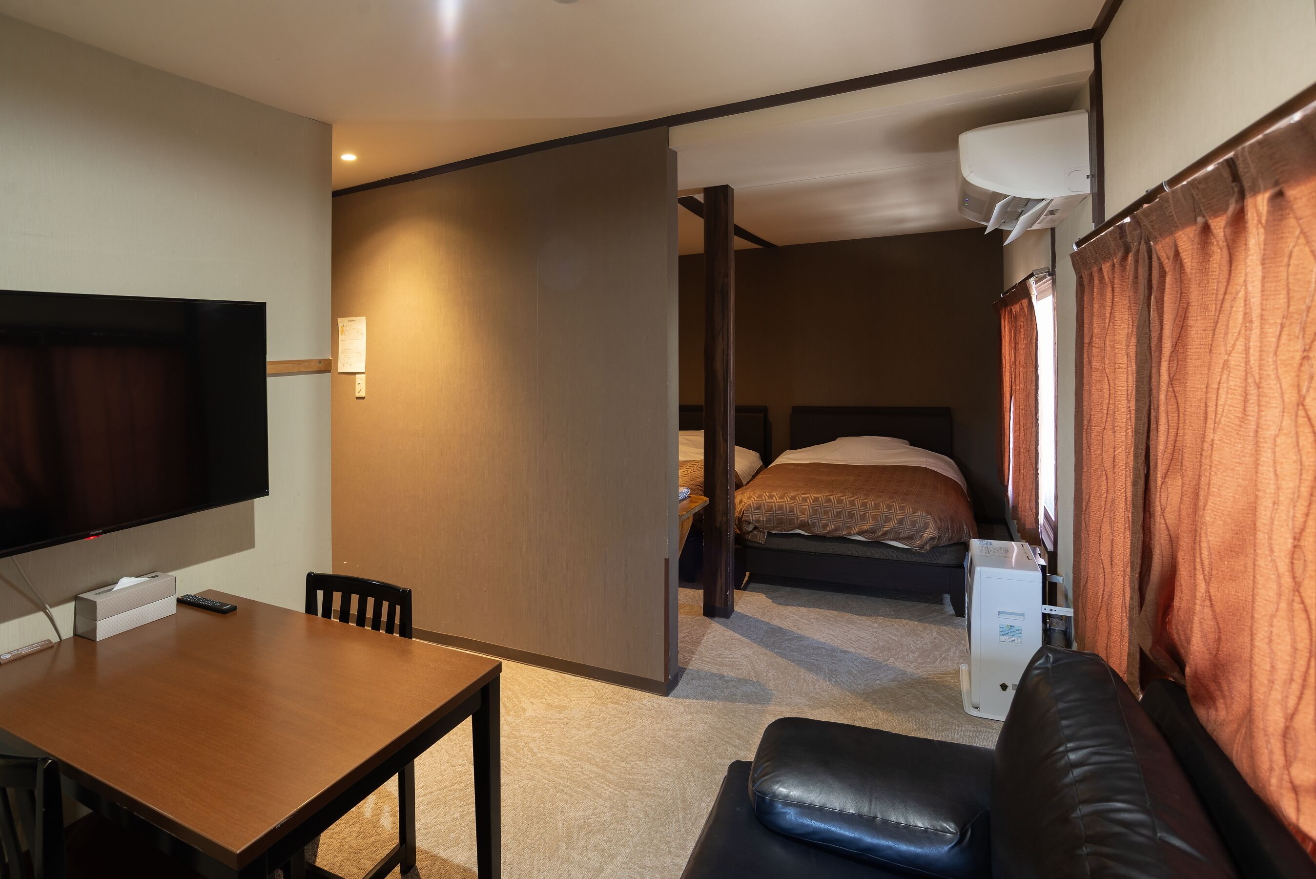 Ein gemütliches Hotelzimmer mit Bett, Schreibtisch mit Stuhl, Fernseher und einer kleinen Küchenzeile.