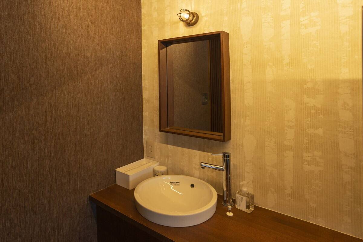 Un baño con tocador de madera, un lavabo blanco, un espejo y una lámpara de pared.