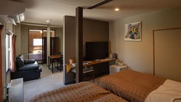 A hotel room with two beds, a desk with a computer, a television, a sofa, and a dining area.