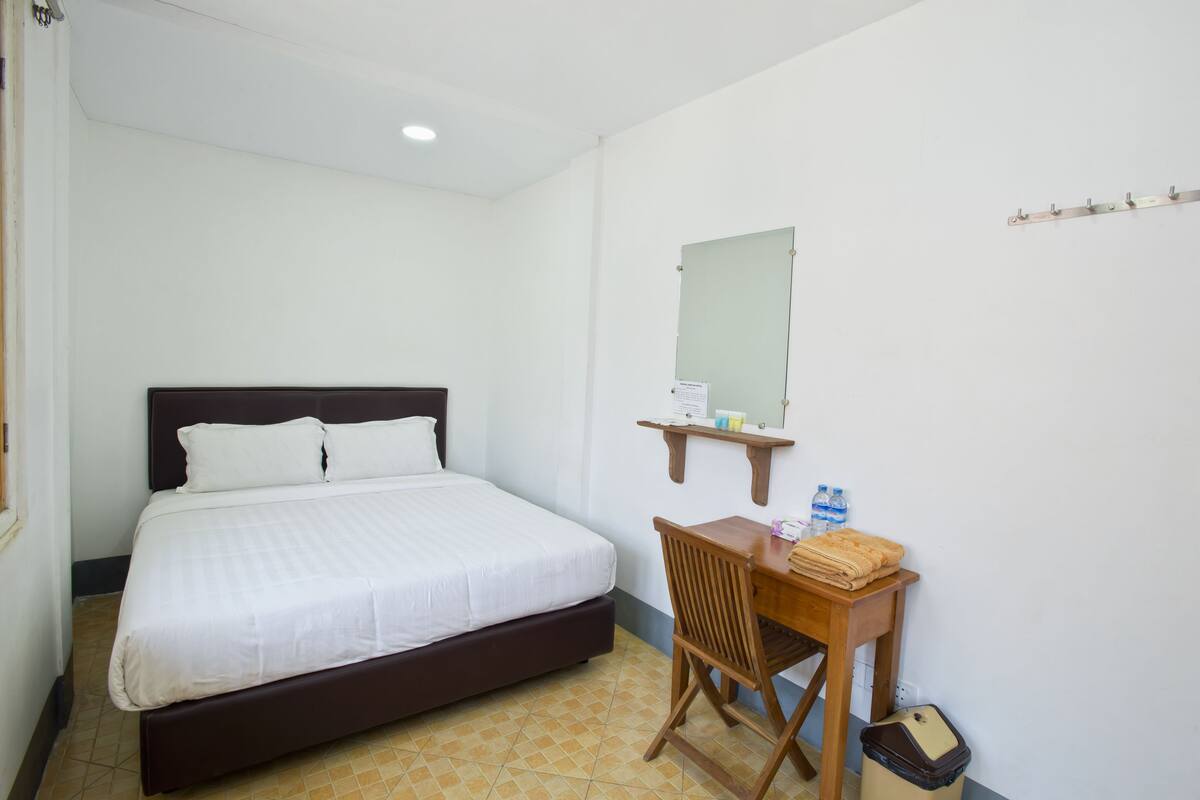 Une chambre d’hôtel comprenant un lit, un bureau avec une chaise, un miroir et une petite étagère avec des articles de toilette.