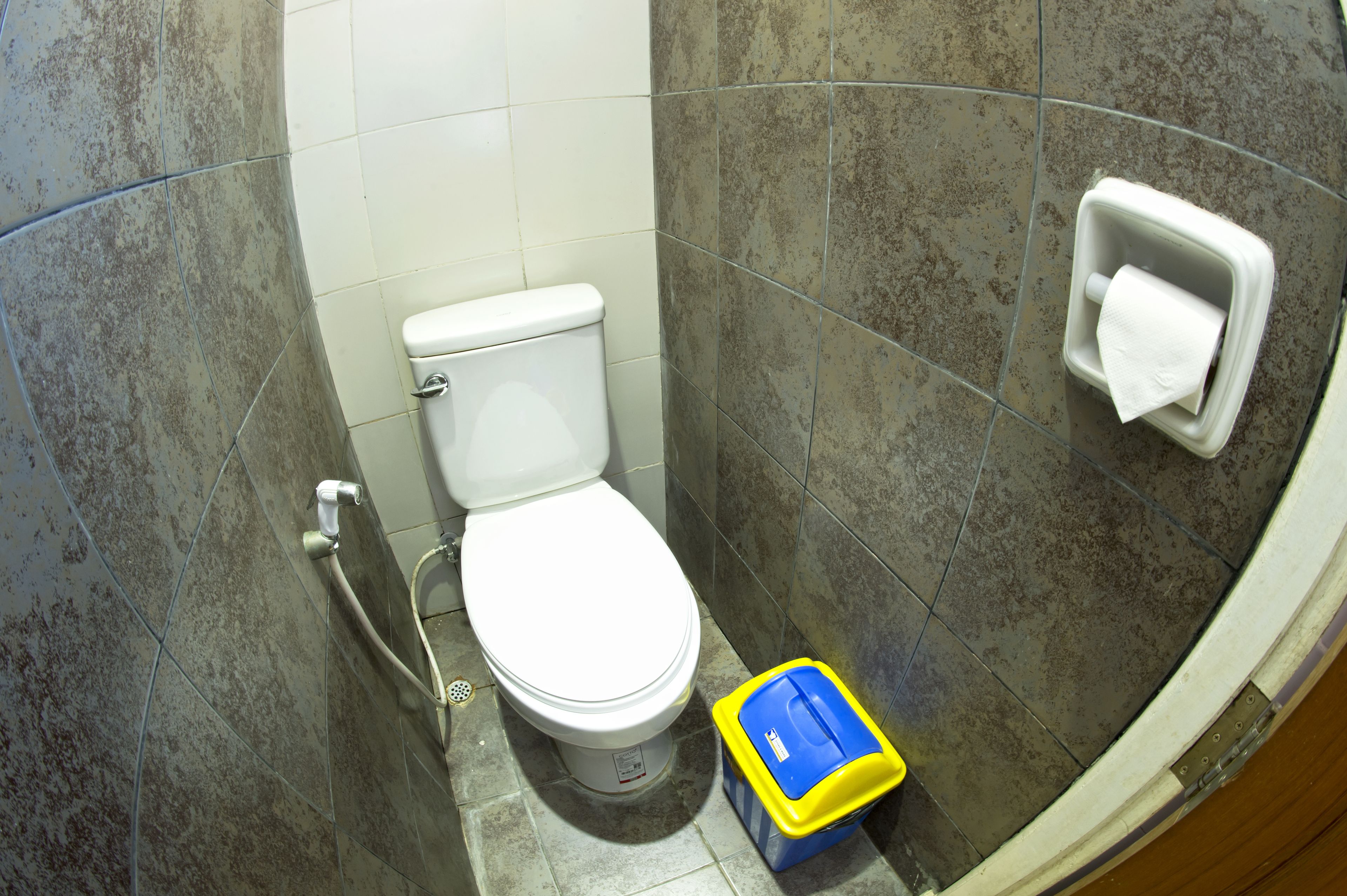 A bathroom with a white toilet, a hand dryer, and a trash bin.