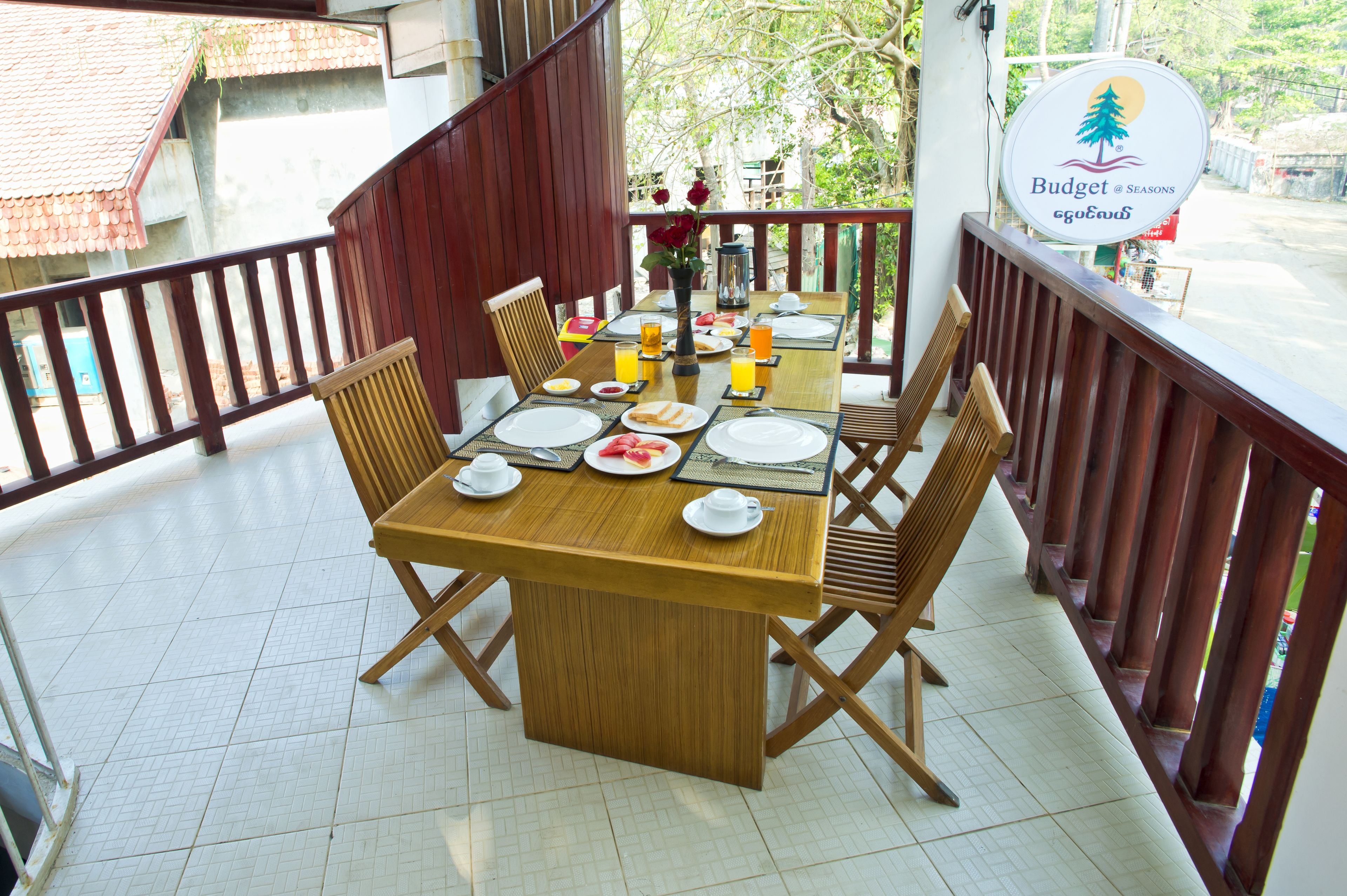 Un comedor con una mesa de madera dispuesta para el desayuno, rodeada de sillas y una barandilla de balcón.
