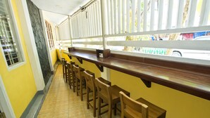 Een restaurant met gele muren, houten barkrukken en uitzicht op de straat door grote ramen.