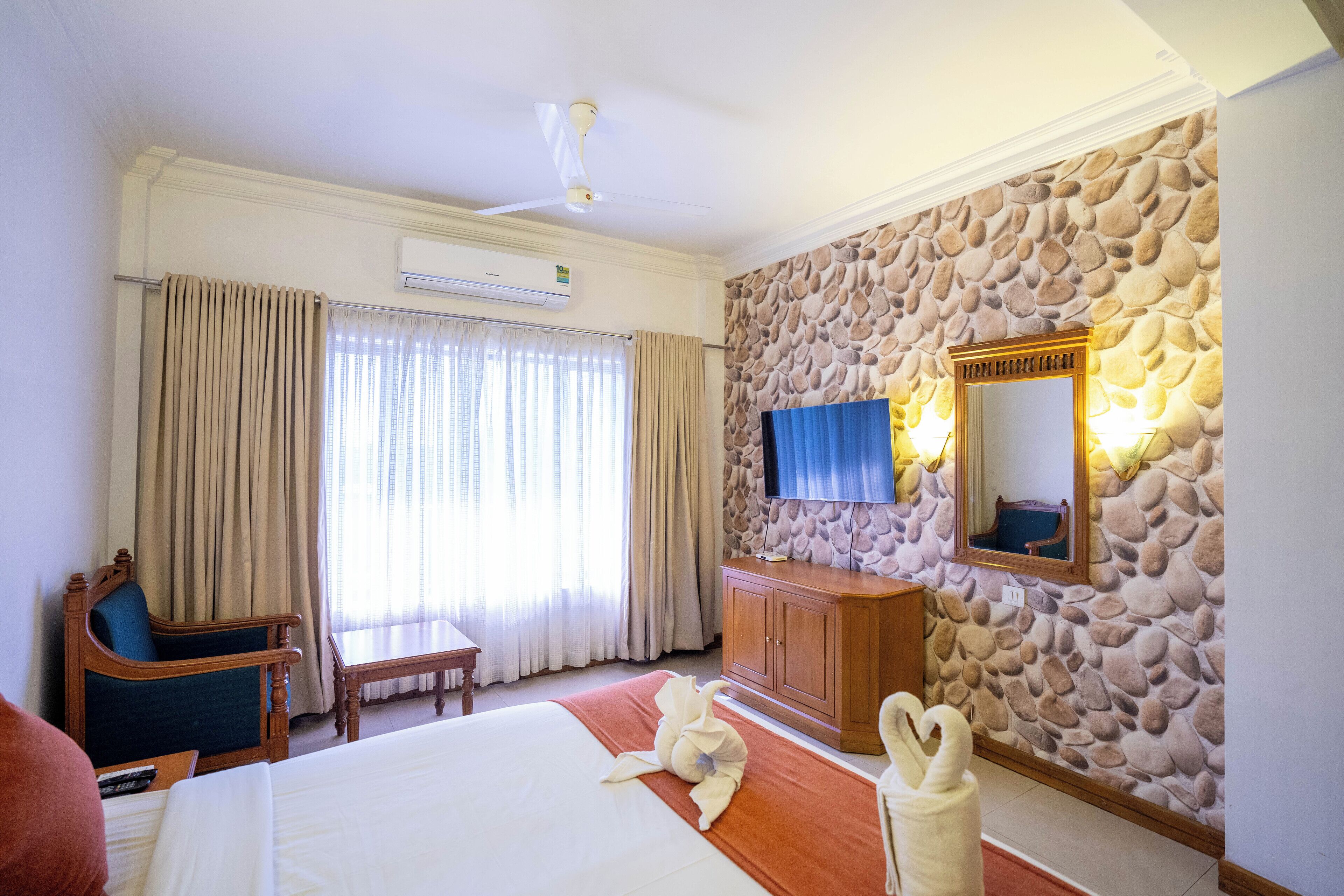 Habitación de hotel con cama, una silla de madera, escritorio, pared de piedra, televisor y aire acondicionado.