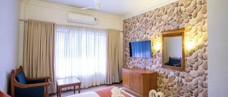 Habitación de hotel con cama, una silla de madera, escritorio, pared de piedra, televisor y aire acondicionado.