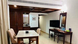 Ein Hotelzimmer mit Essbereich, der einen Marmortisch und Holzstühle, einen Fernseher sowie einen kleinen Tisch mit Spiegel und einigen Gegenständen umfasst.