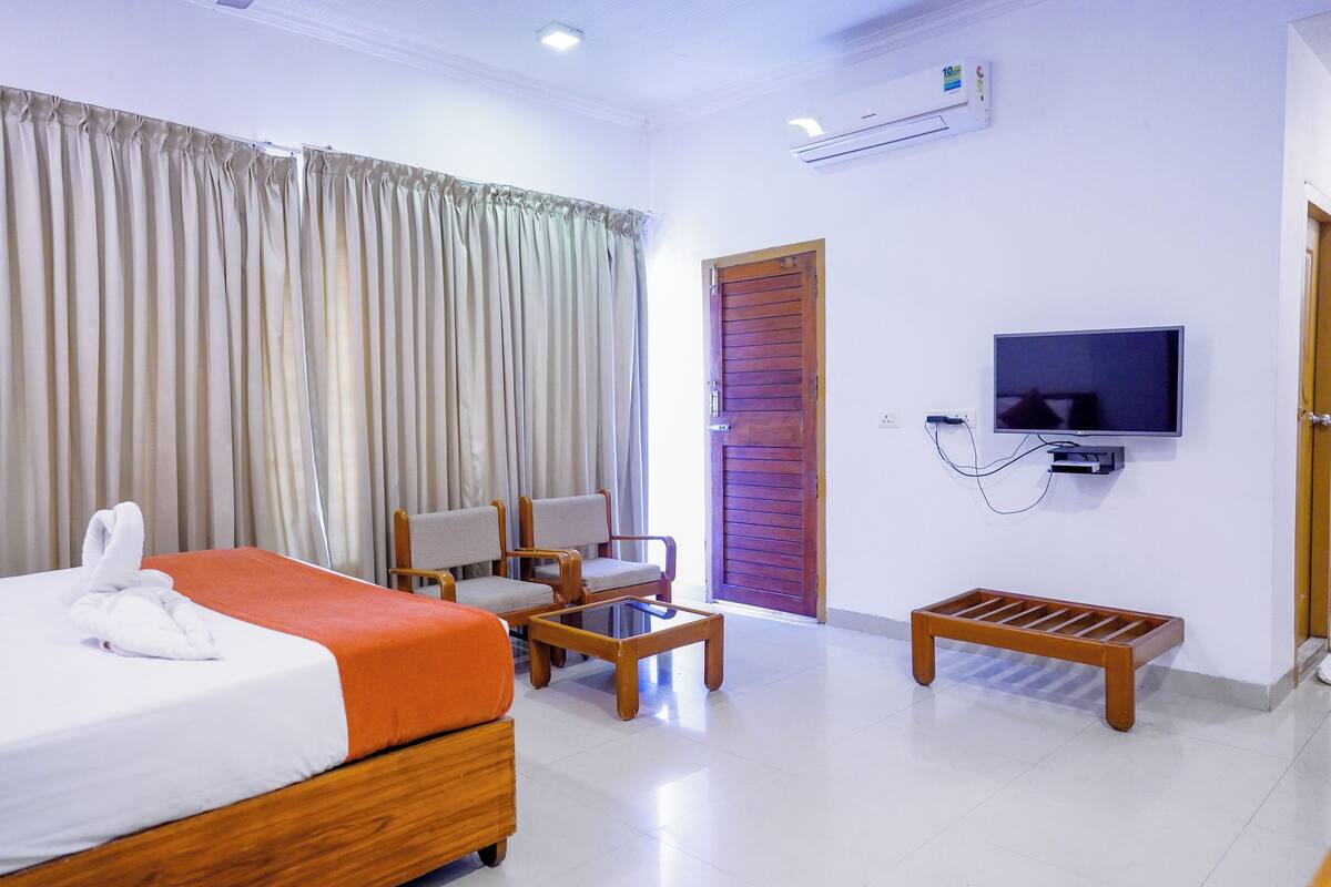 Une chambre d’hôtel comprenant un lit, deux chaises, une table basse, un téléviseur et un petit banc en bois.