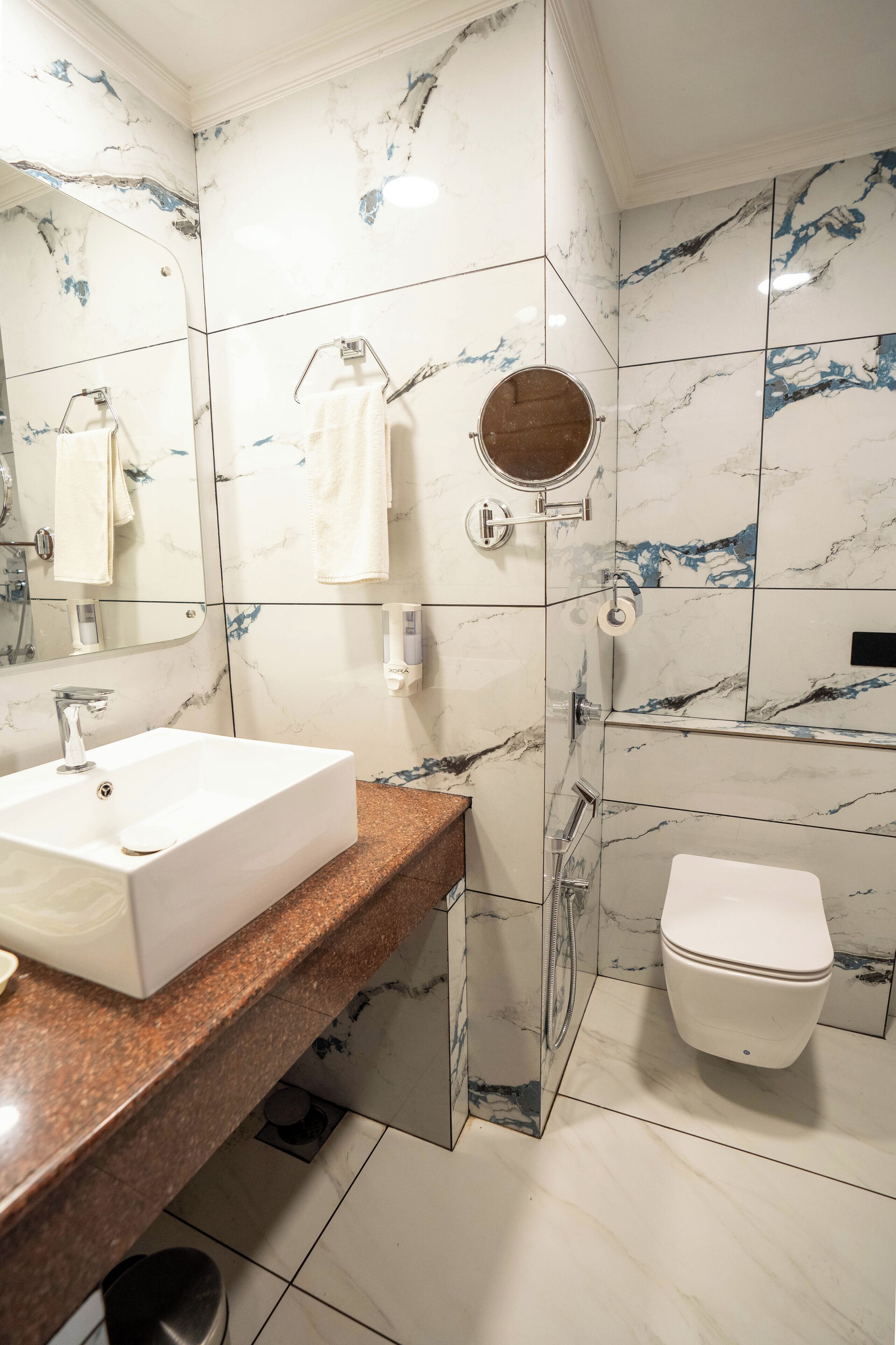 A modern bathroom with a marble backsplash, a white sink, a shower, and a toilet.