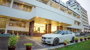 Ein mehrstöckiges Hotel mit weißer Fassade, ein BMW davor geparkt und Kübelpflanzen säumen den Eingang.